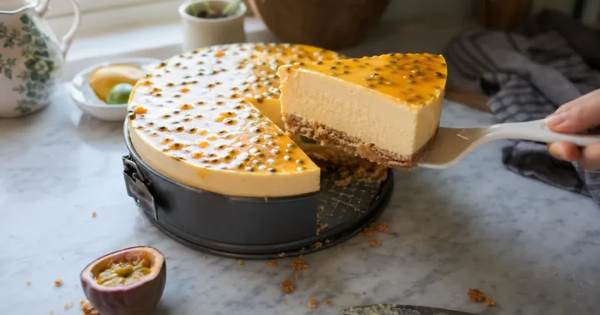 No bake mango-cheesecake med passionsfruktstäcke, en bit upplyft på tårtspade